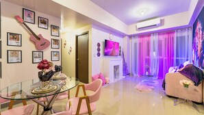 A modern living room with a glass dining table, pink chairs, a pink sofa, and a pink guitar on the wall.
