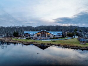 A large, two-story lodge with a prominent entrance and a reflection in the water in front.