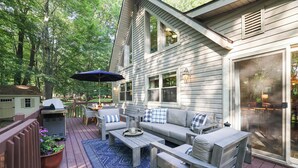 A deck with a sofa, coffee table, and umbrella, surrounded by a wooden deck and potted plants.
