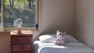A bedroom with a bed, a dresser, a window with a view of trees, and a stuffed animal on the bed.