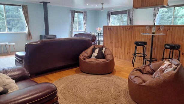 A modern living room with a dark brown sofa, two bean bags, a round woven rug, and a wooden wall. - Yellowstone | quiet country farmhouse | fast internet (Rydal)