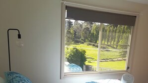A bedroom with a large bed, a bedside lamp, and a window with a view of a green landscape. - Yellowstone | quiet country farmhouse | fast internet (Rydal)
