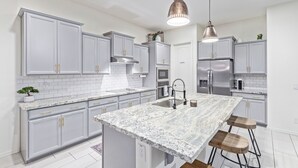 Una cocina moderna con gabinetes grises, una isla grande, electrodomésticos de acero inoxidable e iluminación colgante.