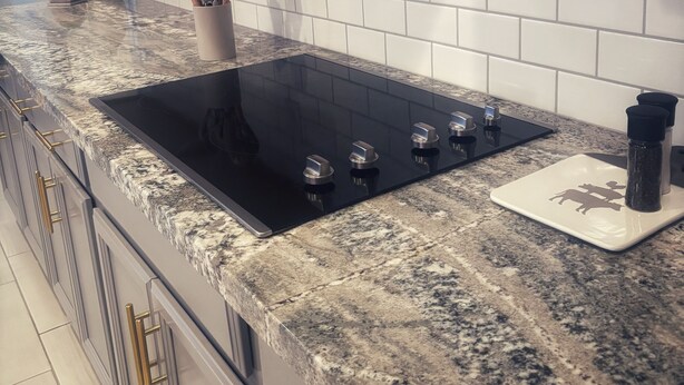 Una cocina con estufa negra, encimera de granito y azulejos blancos tipo metro.
