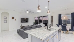 Eine moderne Küche mit Marmorarbeitsplatte und integriertem Spülbecken, ein graues Sofa und ein Deckenventilator.