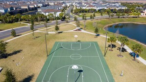 Una pista de bàsquet a l'aire lliure envoltada per una zona residencial amb cases i un carrer.