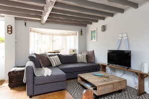Een woonkamer met een grijze bank, een houten salontafel, een televisie en een raam met gordijnen.