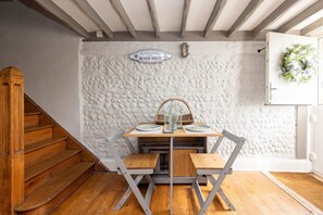 Een houten trap leidt naar een kamer met een wit, gestructureerd muur, een bord met de tekst 'Welcome to the Beach House', een tafel met borden en een glas, en een deur met een krans.