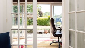 A room with a large open door leading to a garden, a chair, and a small table. - Homely Cottage for 6 Near Chichester Goodwood (Chichester)