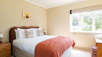 A bedroom with a bed, a nightstand, a dresser, a window with a view of greenery, and a wall-mounted picture.