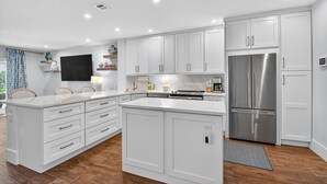 Una cocina moderna con armarios blancos, un refrigerador de acero inoxidable y una isla central con cajones.