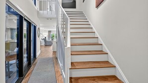 Una escalera moderna con escalones de madera y barandillas blancas, que conduce a un segundo piso con balcón.
