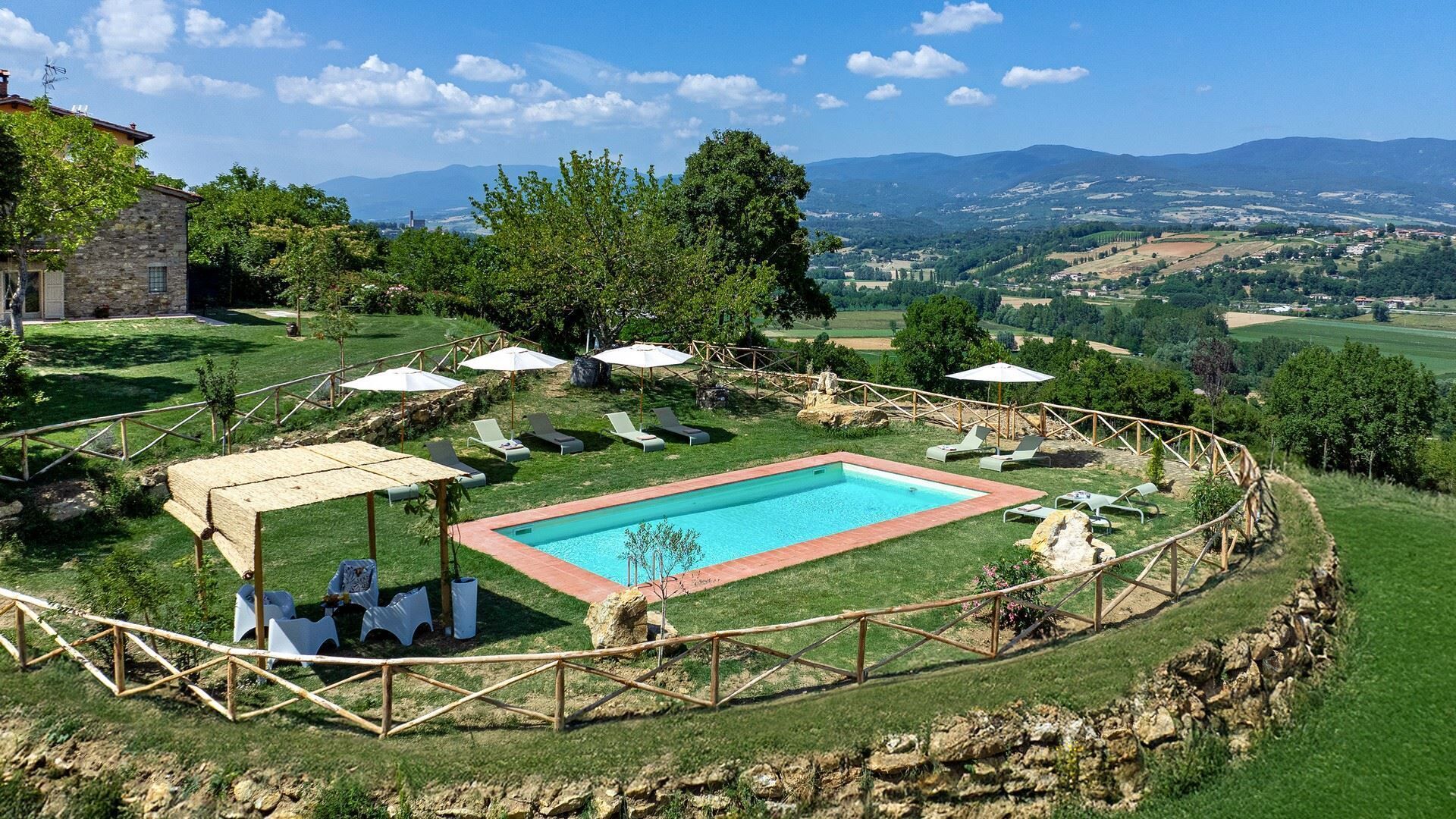 A pool area with a wooden deck, lounge chairs, and umbrellas.