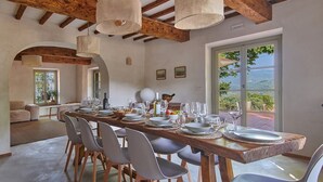 Un'area pranzo con un lungo tavolo in legno apparecchiato per sei persone, circondato da sedie grigie.