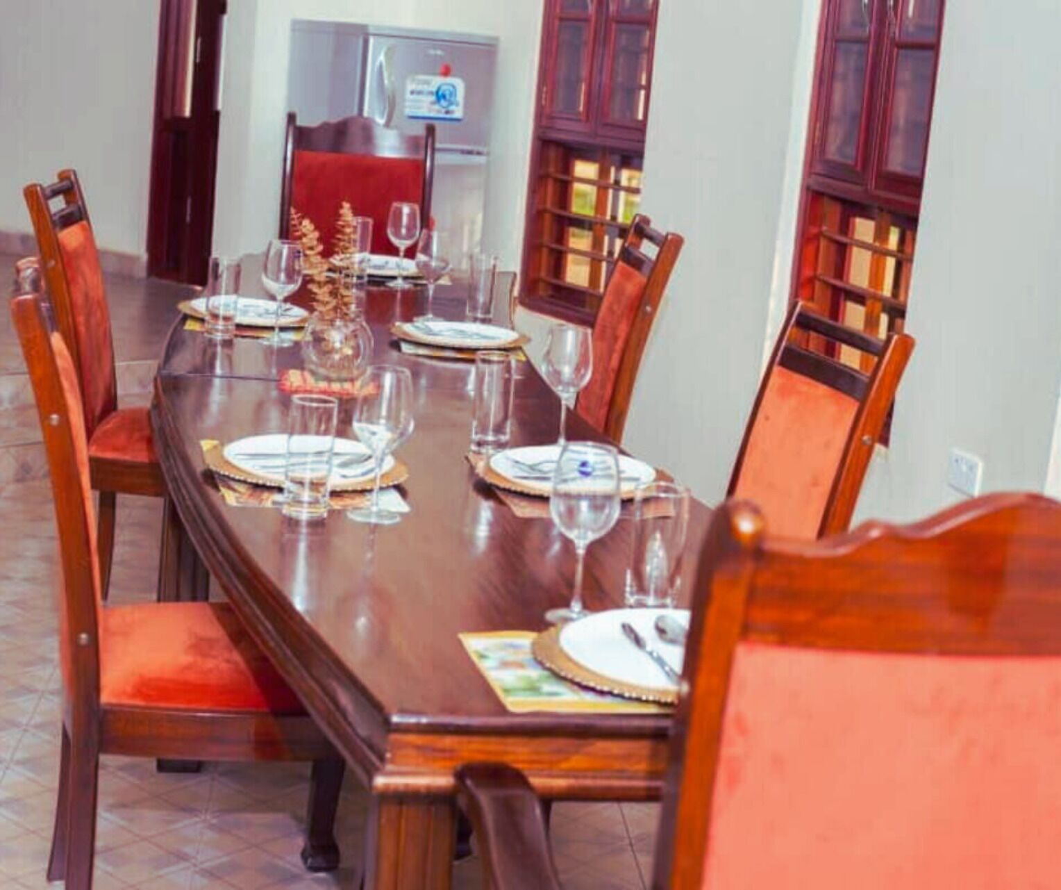 A dining table set for six with chairs, a decorative centerpiece, and a refrigerator in the background.