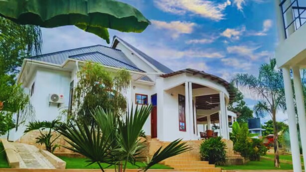 Une maison blanche dotée d’un porche abrité, entourée d’une pelouse bien entretenue et de plantes tropicales.