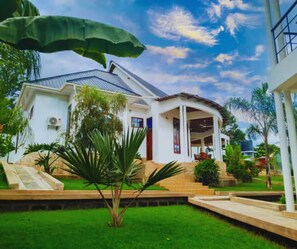 Una casa blanca con porche cubierto, rodeada de un césped cuidado y plantas tropicales.