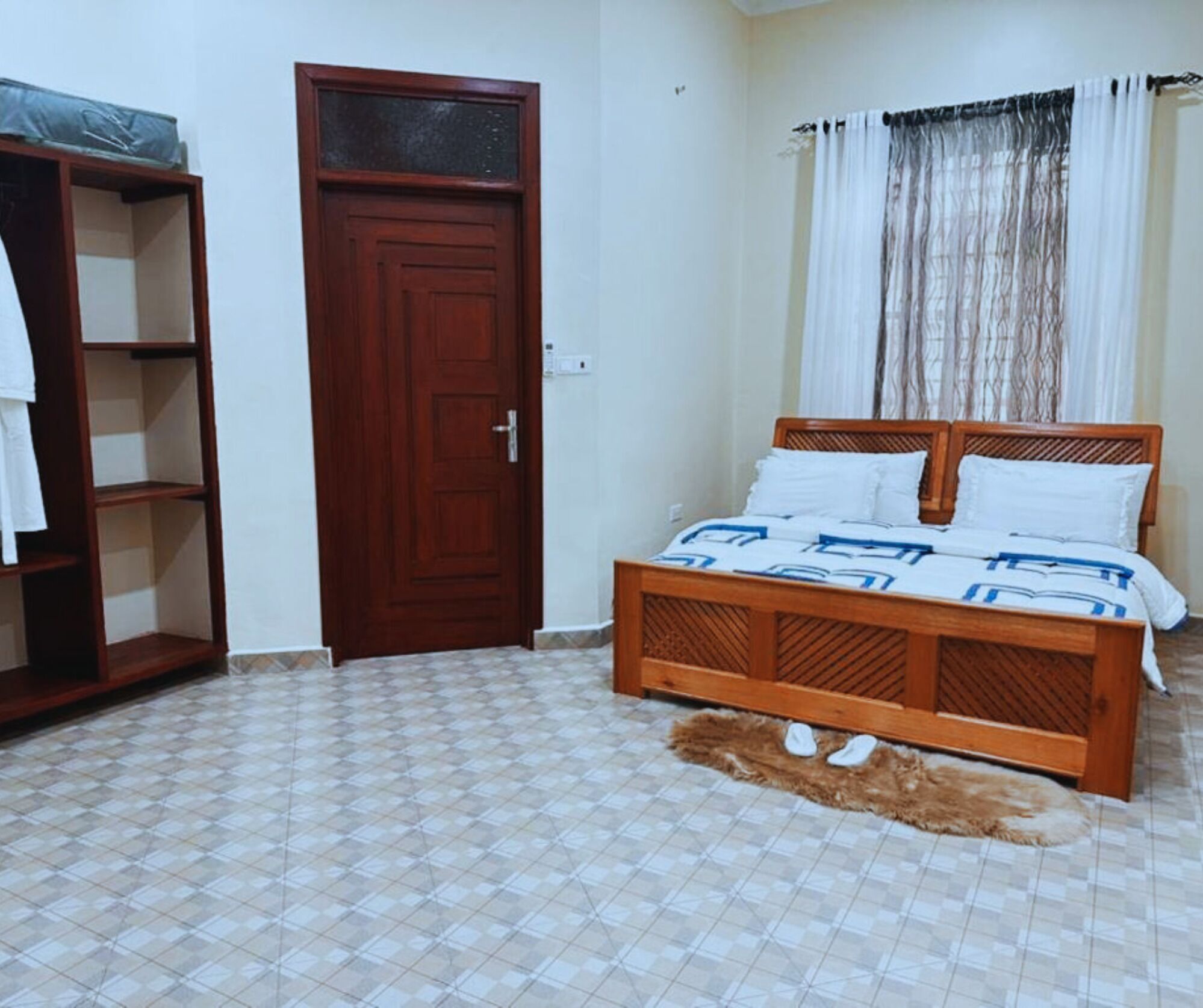 A bedroom with a wooden bed, a wardrobe, a door, and a tiled floor.