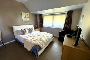 A bedroom with a bed, a desk with a computer, a window with curtains, and a painting on the wall.
