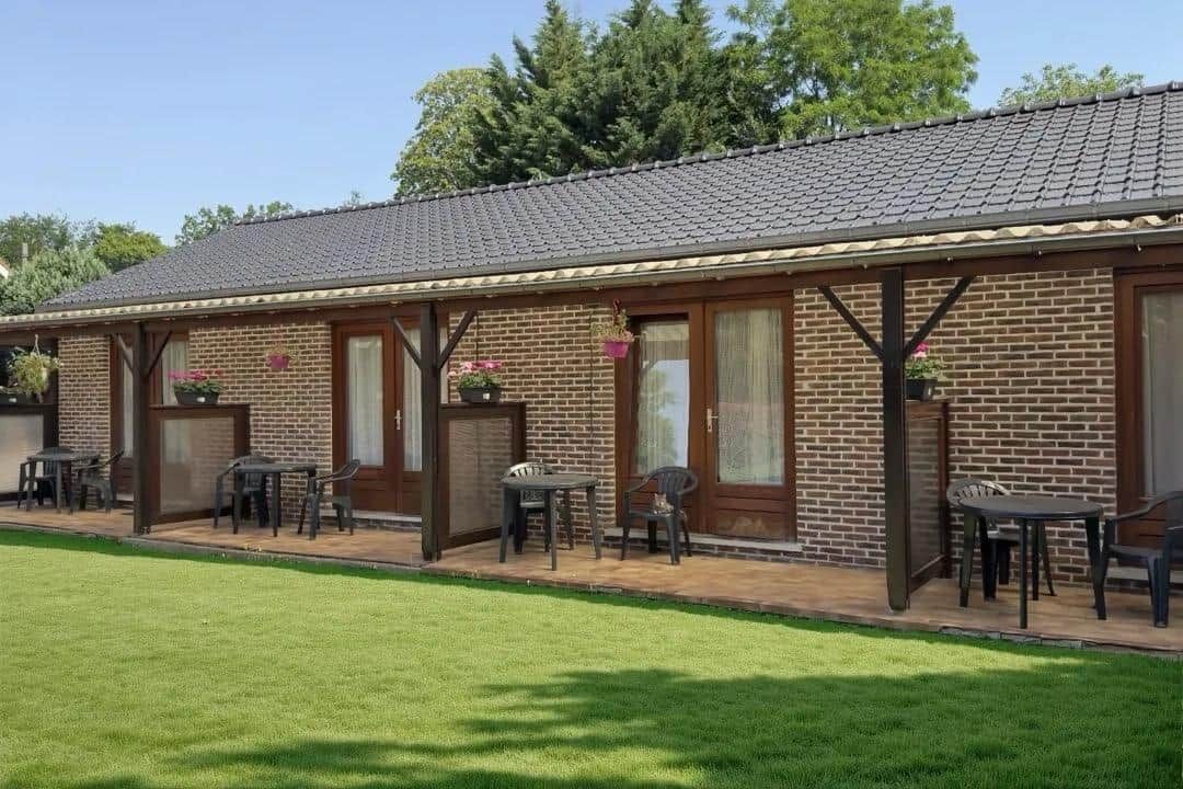 A brick building with a tiled roof, outdoor seating area with tables and chairs, and a well-maintained lawn.