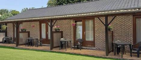 A brick building with a tiled roof, outdoor seating area with tables and chairs, and a well-maintained lawn.