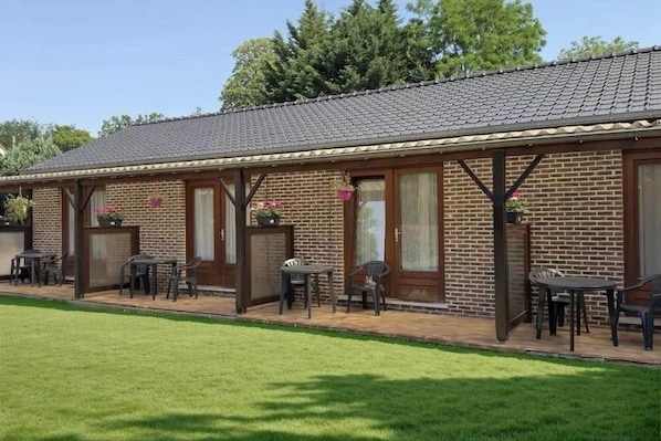 A brick building with a tiled roof, outdoor seating area with tables and chairs, and a well-maintained lawn.