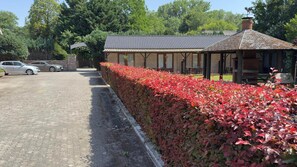 Un bâtiment doté d’un toit recouvert de tuiles, d’une allée pavée et d’une haie aux feuilles rouges.
