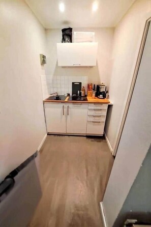 A compact kitchen with white cabinets, a wooden countertop, and a coffee machine.