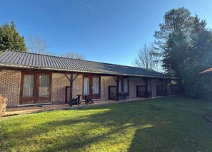 A brick building with a tiled roof, a covered patio, and a grassy yard.