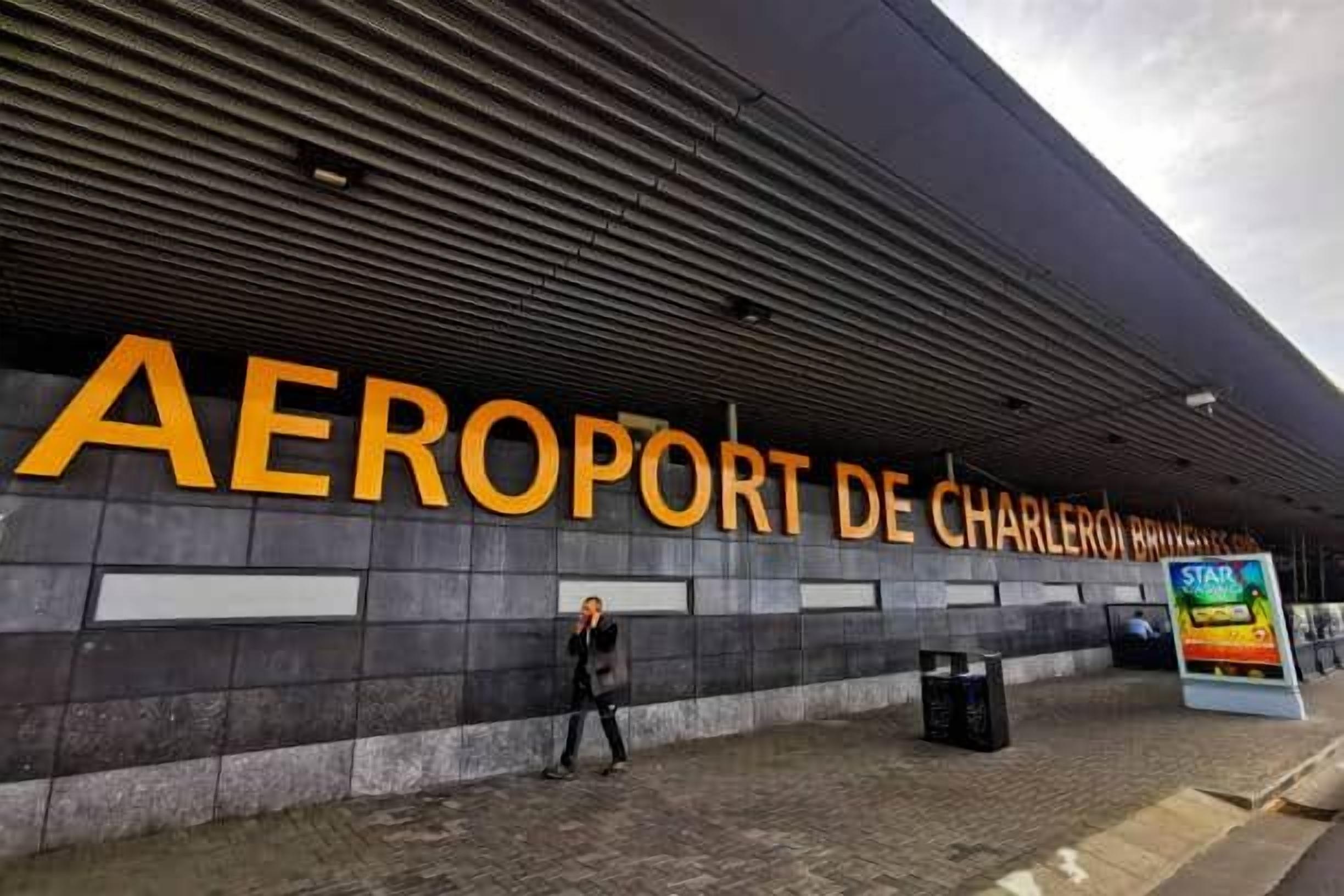 The exterior of the 'AEROPORT DE CHARLEROI BRUSSELS' with a person walking in front.