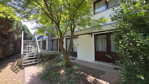 A two-story building with a covered outdoor area, a metal staircase, and a small garden. - Résidence Rachel 29 - Shape - Mons (Mons)