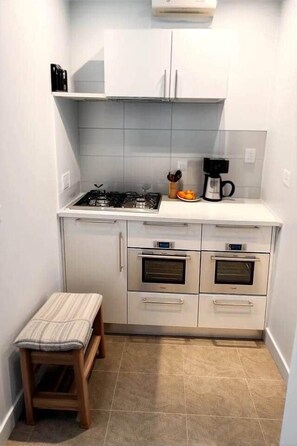 Une cuisine compacte équipée d’une cuisinière à gaz, de deux fours, d’un plan de travail et d’un petit tabouret.
