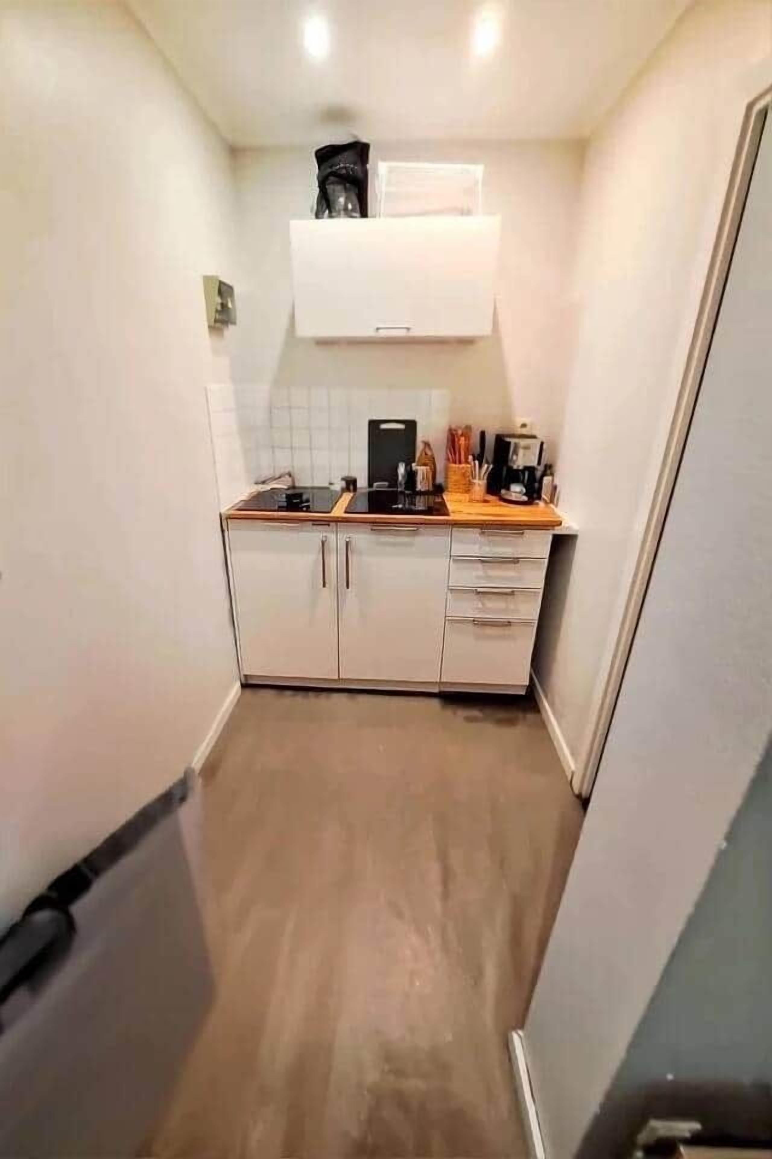 A compact kitchen with white cabinets, a wooden countertop, and a coffee machine.