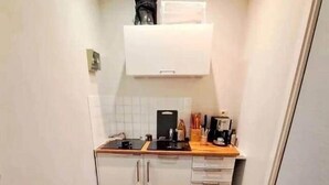 A compact kitchen with white cabinets, a wooden countertop, and a coffee machine.