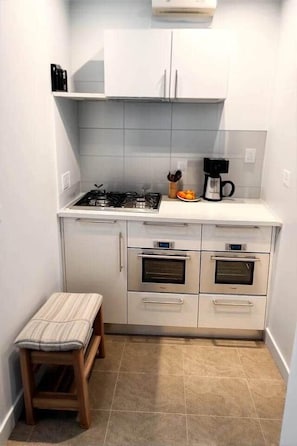 Une cuisine compacte équipée d’une cuisinière à gaz, de deux fours, d’un plan de travail et d’un petit tabouret.
