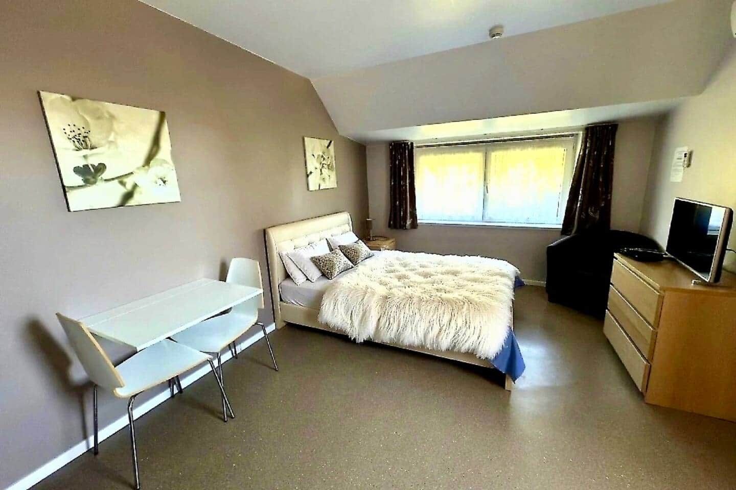 Ein Schlafzimmer mit einem Bett, einem Schreibtisch, einem Stuhl, einer Kommode und einem Fernseher.