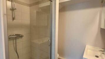 Une salle de bain avec une douche à parois de verre, un lavabo blanc et un sol carrelé.