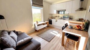 Une cuisine moderne avec des meubles blancs, un coin repas avec une table et des chaises en bois, et un salon avec un canapé et un tapis.