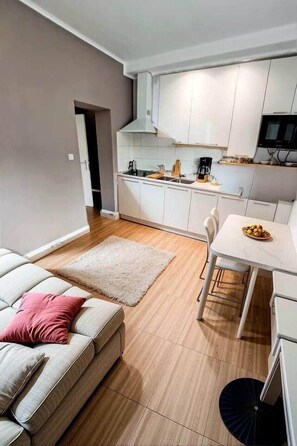 Une cuisine moderne avec des meubles blancs, une table à manger et un canapé agrémenté d’un coussin rose.