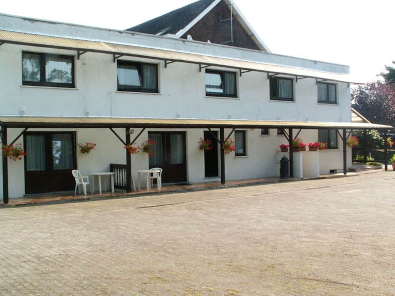 Een gebouw met twee verdiepingen, een overdekte patio, buitenzitplaatsen en bloembakken.