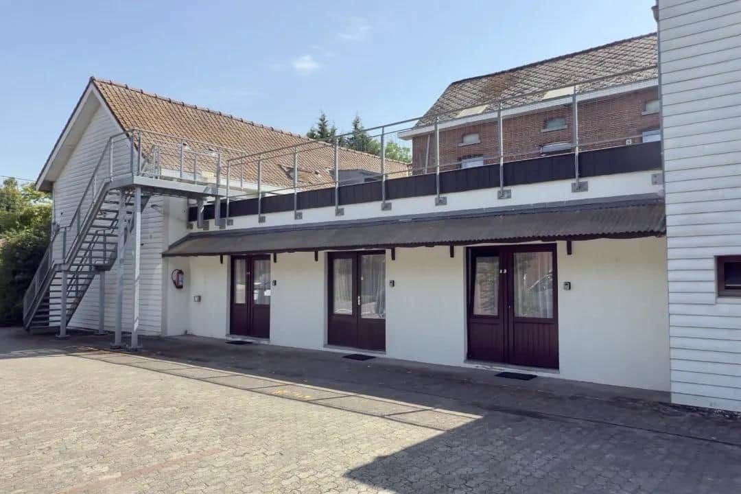 Een gebouw met twee verdiepingen, een overdekte veranda, een trap naar een hoger gelegen niveau en een buitenkraan op de begane grond.