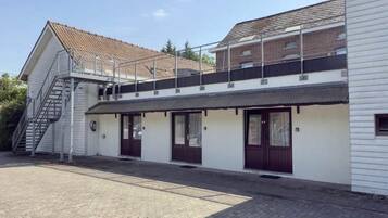 Een gebouw met twee verdiepingen, een overdekte veranda, een trap naar een hoger gelegen niveau en een buitenkraan op de begane grond.