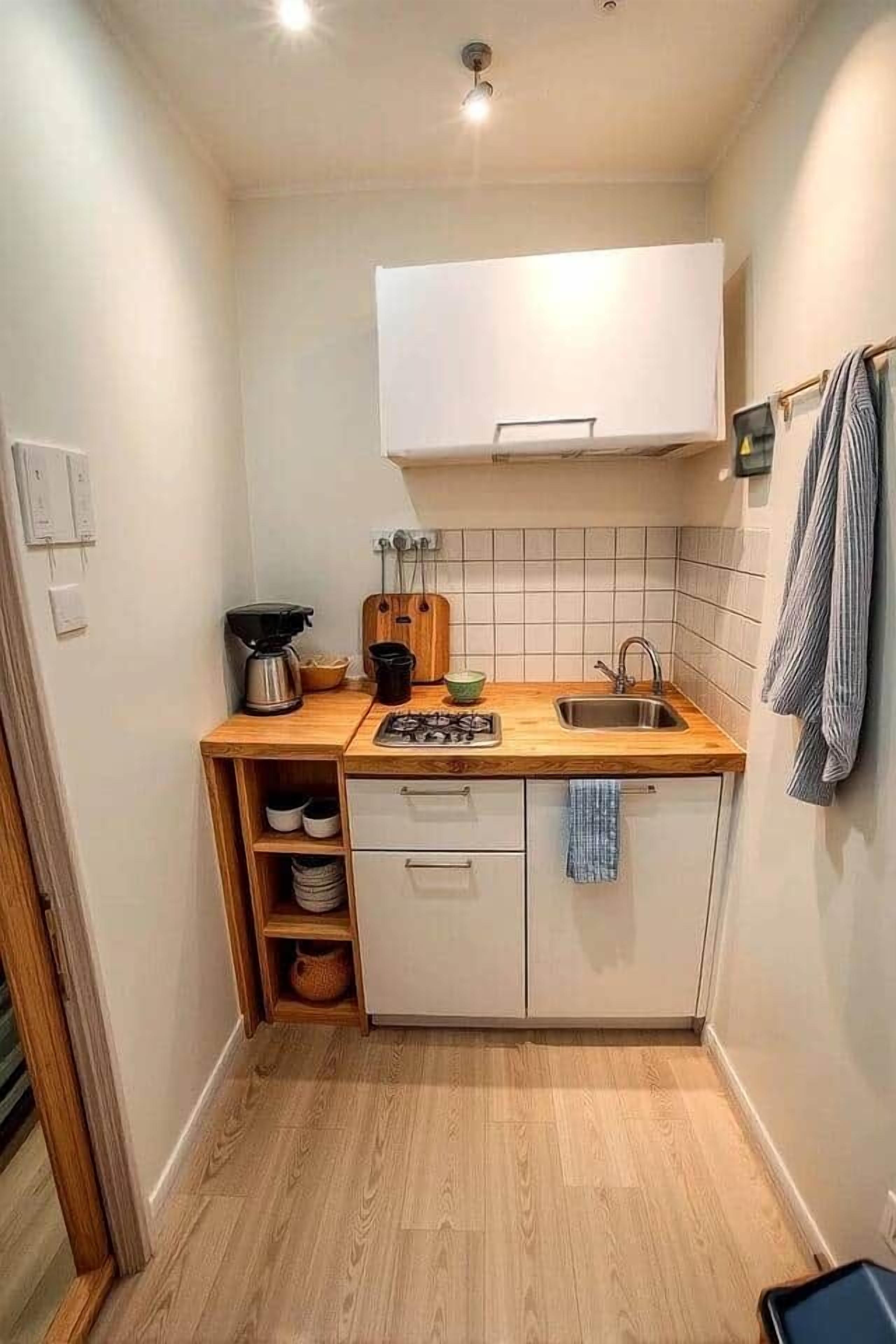 Een kleine keuken met een houten aanrecht, een spoelbak, een fornuis en een wit kastje erboven.