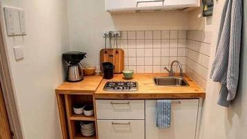 Een kleine keuken met een houten aanrecht, een spoelbak, een fornuis en een wit kastje erboven.