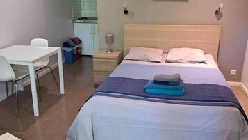 Un dormitorio con cama, escritorio y silla. También hay una mesita y una mesita de noche con una lámpara.
