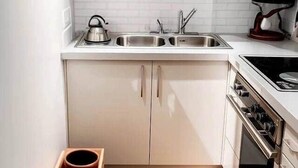 A compact kitchen with white cabinets, a stainless steel sink, a kettle, and a built-in oven.
