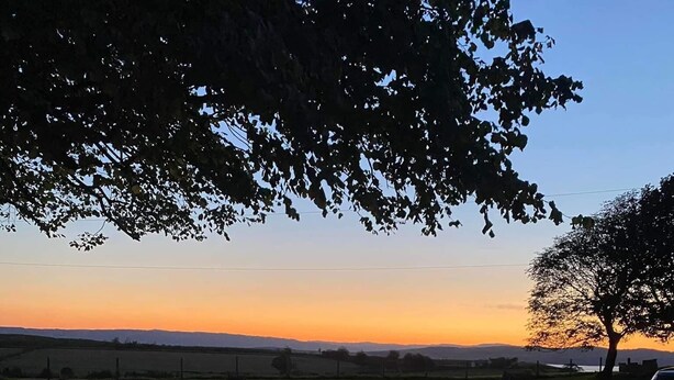 Una vasca idromassaggio con vista su un tramonto e un albero.