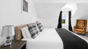 Una camera d'albergo con un letto, una sedia, una lampada e una finestra con tende.