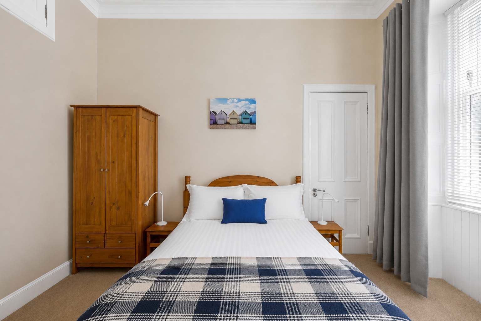 Ein Schlafzimmer mit einem Bett, einem Holzschrank, einem Gemälde, einer Tür und Vorhängen.
