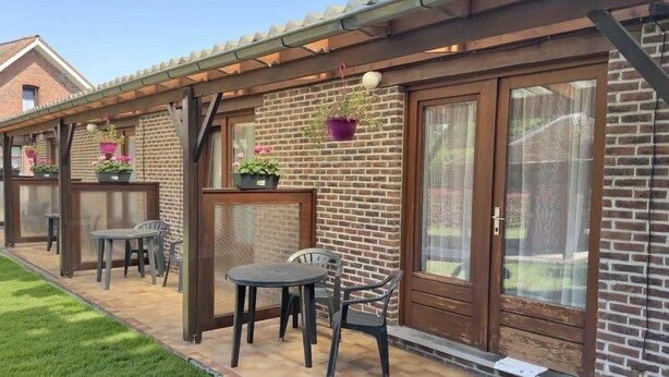 A patio area with a brick wall, a wooden pergola, and outdoor furniture.